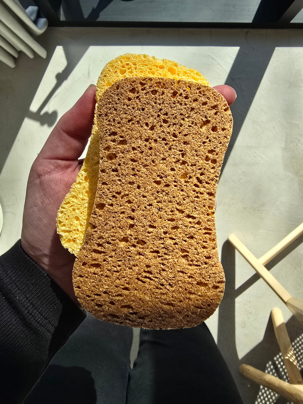 Twee natuurlijke sponzen met een gele cellulosezijde en bruin schuurdeel, in de hand gehouden